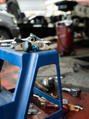 Dynamic view of a workshop with tools and automotive parts on a stool, inside a repair shop.