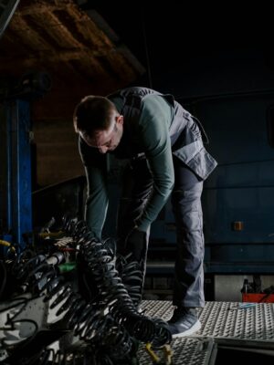 Mechanic bending over to repair truck inside a dimly lit garage, demonstrating precision.