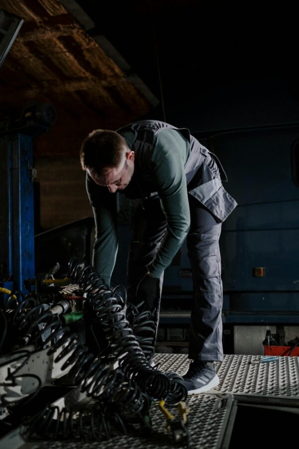 Mechanic bending over to repair truck inside a dimly lit garage, demonstrating precision.