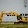 Yellow Komatsu excavator at an outdoor construction site beside a grey building wall.