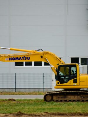 Yellow Komatsu excavator at an outdoor construction site beside a grey building wall.