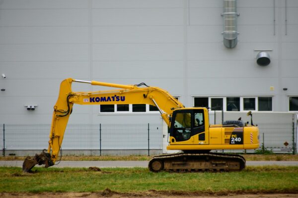 Yellow Komatsu excavator at an outdoor construction site beside a grey building wall.